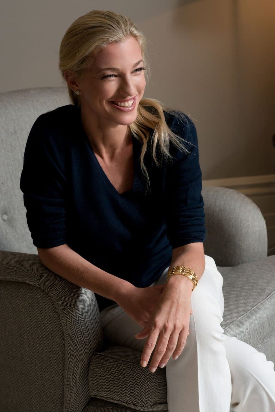 Nicole Junkermann seated in an armchair in a navy top and white trousers, smiling in conversation