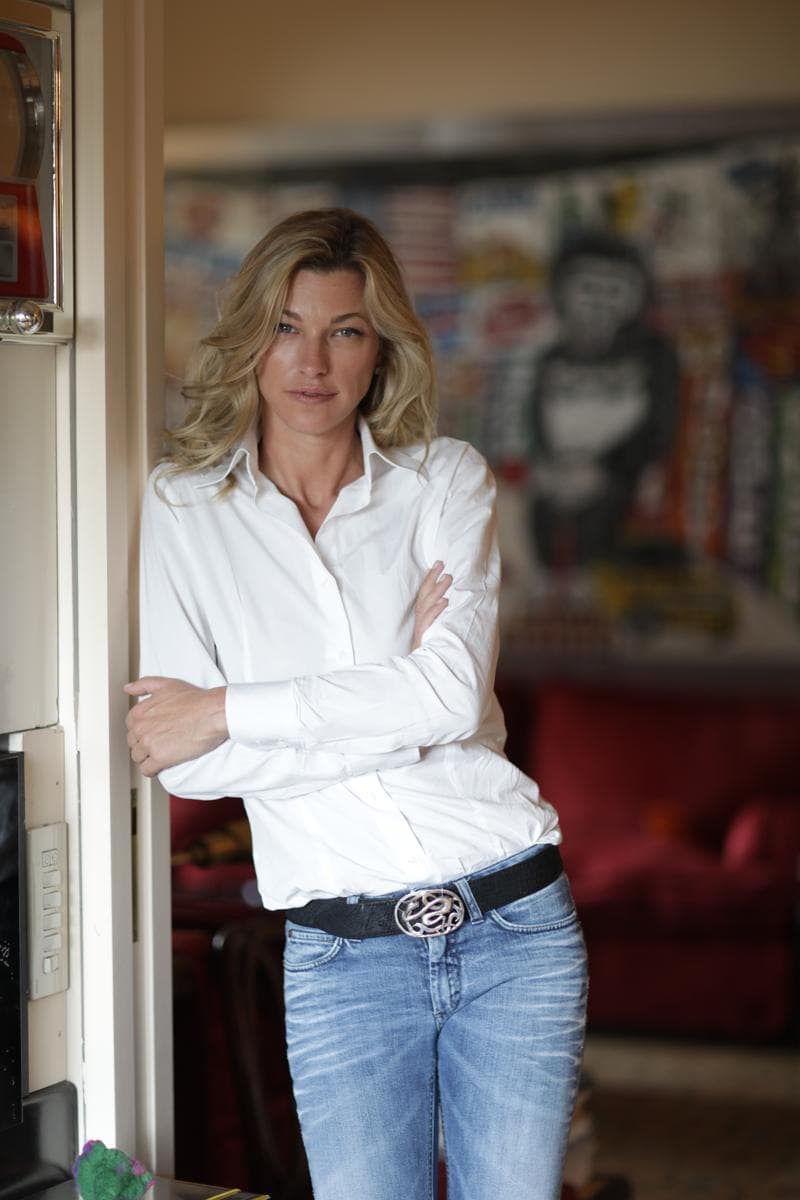 Nicole Junkermann in a white shirt and jeans, leaning in a doorway beside colourful modern art at home