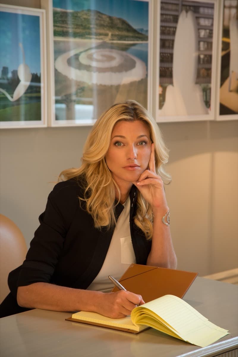 Nicole Junkermann writing in a notebook at a lamp-lit desk, a thoughtful editorial portrait